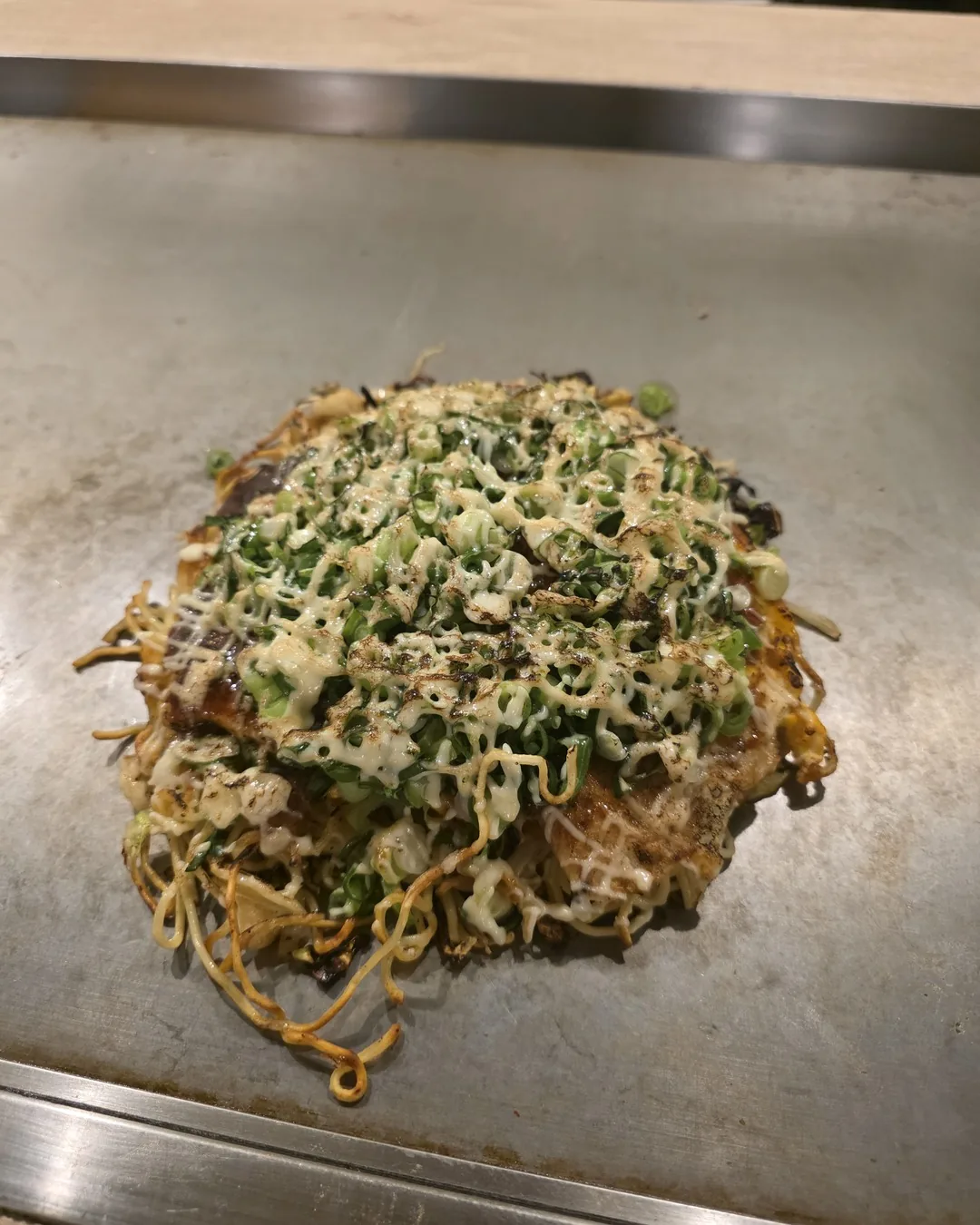 Okonomiyaki estilo Hiroshima na chapa, com macarrão yakisoba e cebolinha por cima